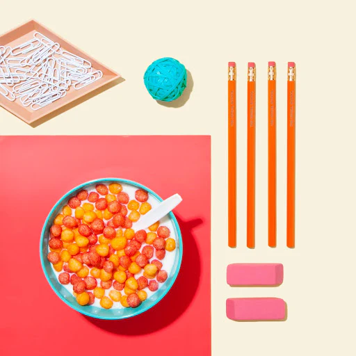 Schoolyard Snacks Keto Fruity Cereal with milk in a bowl, surrounded by colorful stationery supplies.